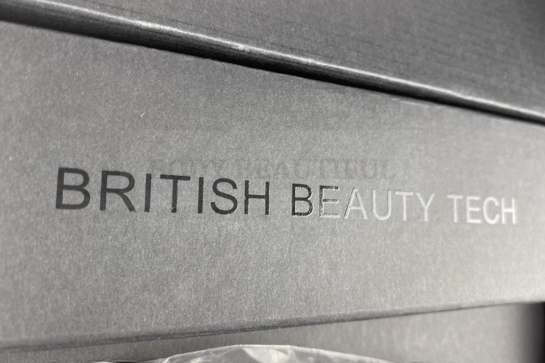 Embossed 'Brtitish Beauty Tech" on the top of the cardboard securing the power cable