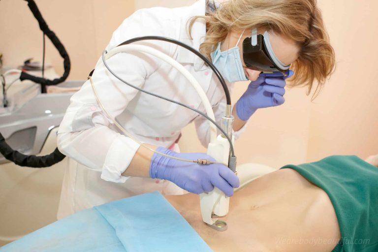 A professional laser hair removal operative wearing gloves, mask and safety glasses lasers a ladies tummy and bikini line.